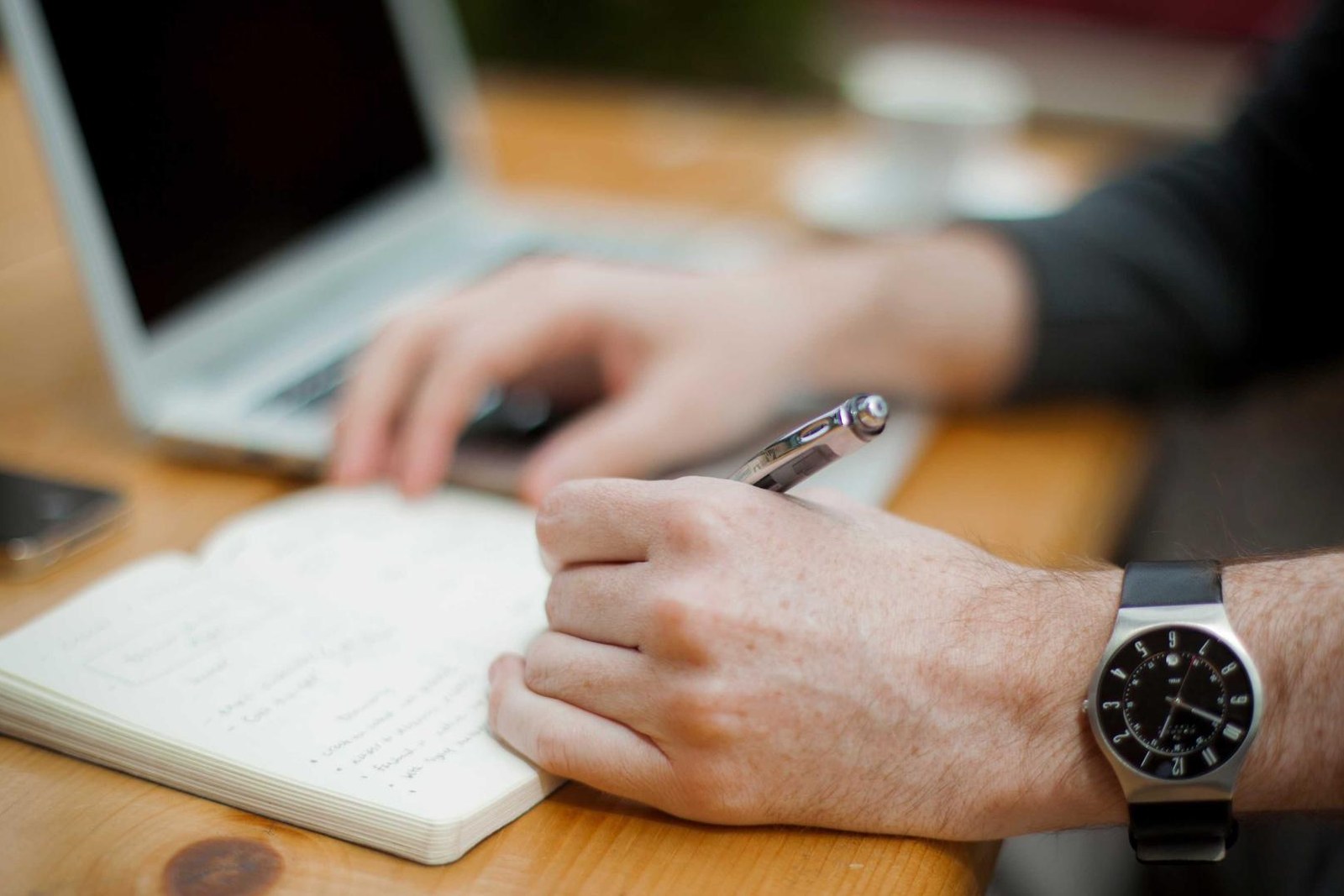 Editorial context photograph of a person writing beside a laptop